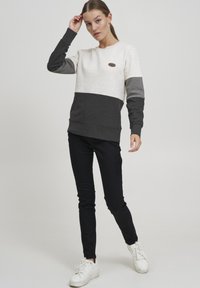 Harmaa ja beige collegepaita, jossa on lohkoväriasettelu, pitkät hihat ja pyöreä kaula-aukko. Yhdistetty mustiin housuihin ja valkoisiin lenkkareihin.