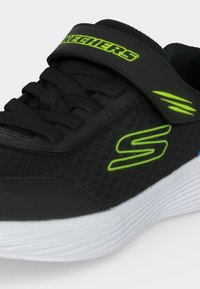 Μαύρο αθλητικό παπούτσι Skechers με φωσφορίζοντα πράσινα λογότυπα, λουράκι βέλκρο, μαύρα κορδόνια και λευκή σόλα.