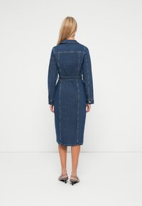 Τζιν φόρεμα με συρρικνωμένη μέση, μακριά μανίκια και μήκος μέχρι το μέσο. Διαθέτει ραφές και γιακά με εγκοπή. Σκούρο μπλε χρώμα.