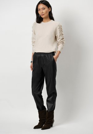 Beige sweater with ruched sleeves, paired with black leather pants and brown ankle boots. Simple design, soft texture, and modern silhouette.