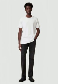 White short-sleeve T-shirt with a small logo on the chest, paired with dark gray trousers and black shoes. Simple, casual design.