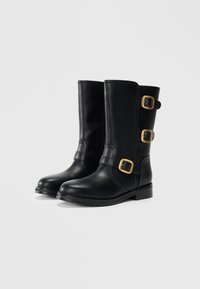 Botas de cuero negro hasta la rodilla con punta redondeada, detalles de doble hebilla y un tacón bajo y cuadrado. Textura suave y construcción resistente.
