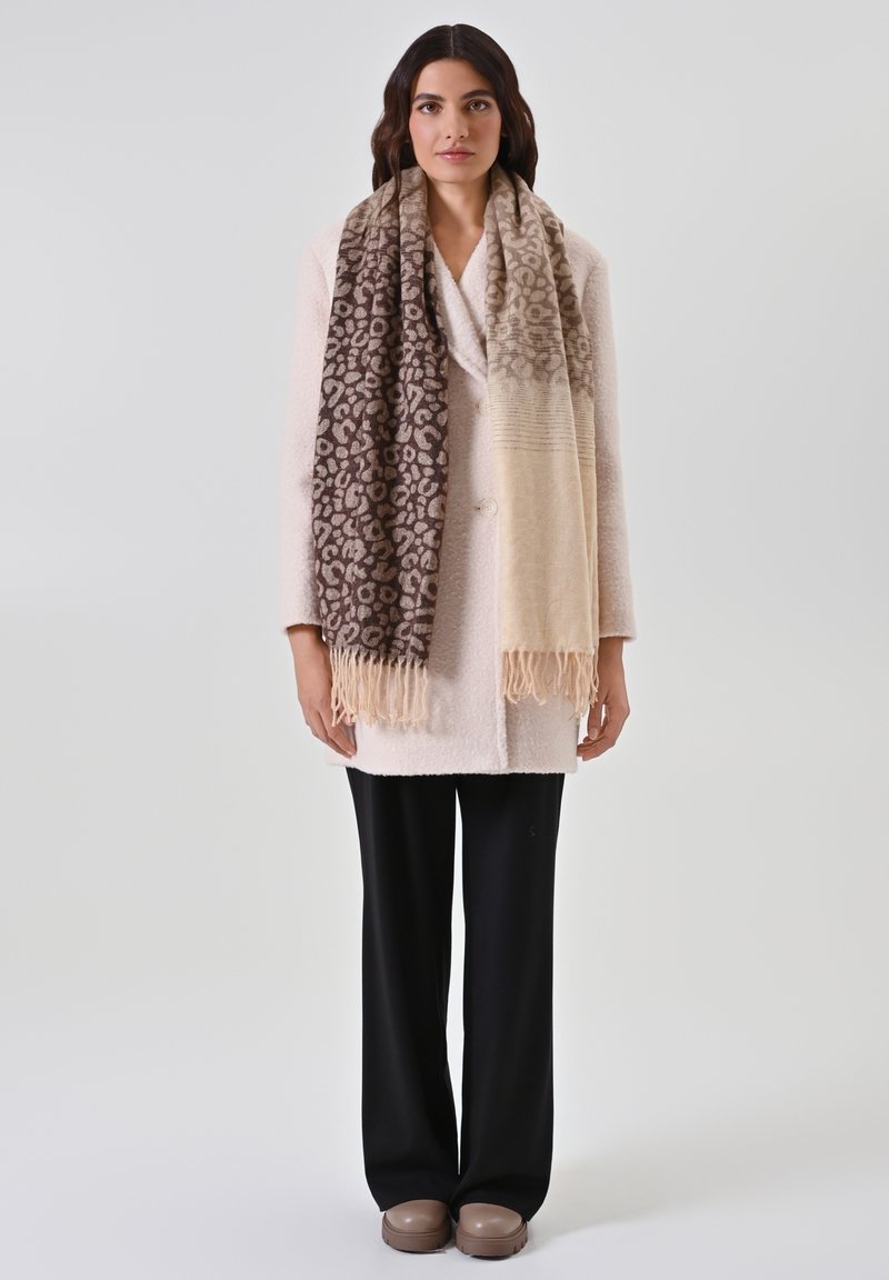 Cappotto crema, sciarpa a motivo leopardato marrone e beige con frange, pantaloni neri a gamba larga e calzature taupe. Design semplice e texture.