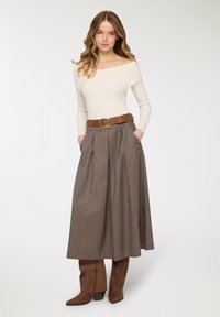 Gonna lunga marrone con motivo a pieghe, abbinata a un top crema scollato sulle spalle. Cintura marrone con fibbia rotonda e stivali marroni fino al ginocchio.