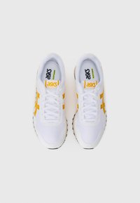 Pair of white and yellow Asics sneakers with laces, viewed from above against a plain white background.