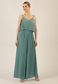  geplooide teal jumpsuit met dunne verstelbare bandjes en laagjesontwerp. De stof heeft een zachte textuur en de outfit heeft een vloeiende silhouet.