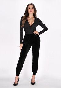 Zwarte longsleeve bodysuit met een diepe V-hals en een voorste twistdetail, gecombineerd met hoge taille, taps toelopende zwarte fluwelen broek.