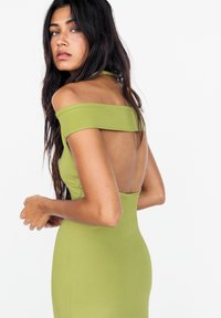 Robe verte décolletée avec une silhouette ajustée, un design sans dos, une texture lisse et des lignes épurées. Présente un éclat subtil.