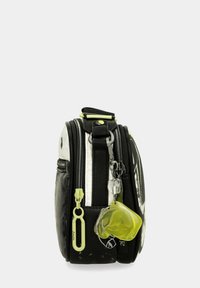 Bolso texturizado en blanco y negro con múltiples compartimentos con cremallera, un asa superior y un llavero amarillo como acento. Presenta un acabado brillante y detalles de hardware.