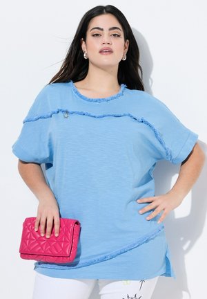 Svetle modré oversized tričko s třepenými okraji a krátkými rukávy, doplněné růžovou prošívanou kabelkou. Hladká textilie, uvolněný střih.