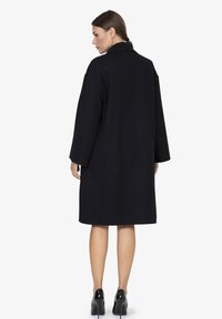 Cappotto in lana nera con vestibilità regolare, maniche larghe e colletto. Il retro è semplice, con un design lungo fino al ginocchio.