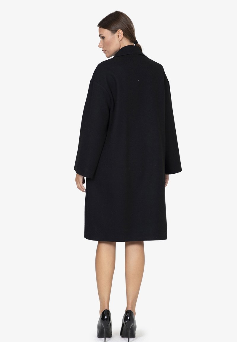 Cappotto in lana nera con vestibilità regolare, maniche larghe e colletto. Il retro è semplice, con un design lungo fino al ginocchio.