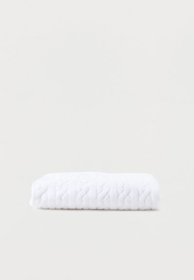 Λευκή διπλωμένη πετσέτα με διακριτικό ανάγλυφο μοτίβο σε απλό ανοιχτό φόντο.