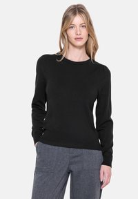 Maglione nero realizzato in materiale morbido, con scollatura rotonda e maniche lunghe con dettagli a palloncino, abbinato a pantaloni grigi.