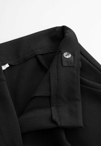 Czarny materiał o gładkiej fakturze, złożony na brzegu z srebrnym guzikiem. Na krawędziach widoczne są szczegóły szwów.