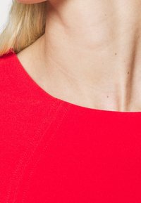 Czerwona dopasowana bluzka z okrągłym dekoltem i widocznymi detalami szwów. Materiał wydaje się gładki z delikatnym połyskiem.