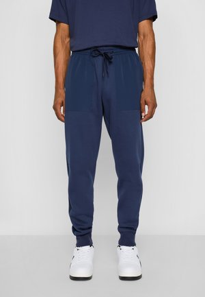 Pantalones jogger azul marino hechos de tejido suave, con una cintura ajustable y dos grandes bolsillos delanteros con textura contrastante.