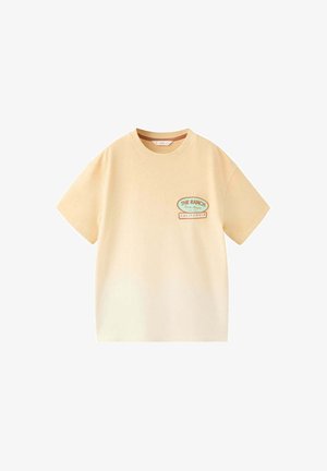 Beige kortærmet T-shirt med "The Ranch Santa Monica L.A. U.S. California"-patch på venstre bryst, rund hals.