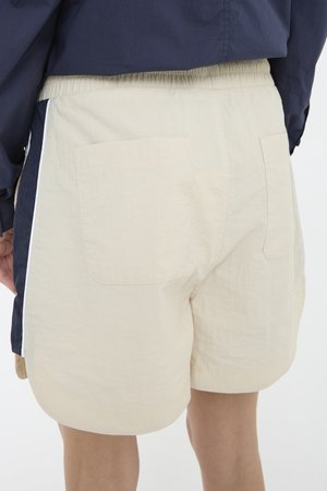 Beige shorts met een ontspannen pasvorm, een elastische tailleband en twee achterzakken. Zijkant streepdetail in marineblauw. Lichtgewicht, gestructureerde stof.