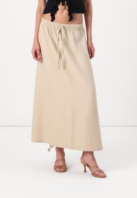 Falda maxi beige con cintura elástica y cordón, de corte recto y fabricada en tela ligera. Se lleva con tacones con tiras.