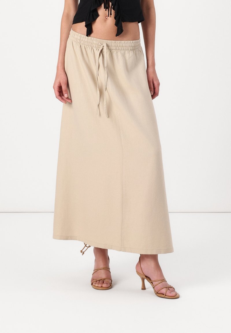 Falda maxi beige con cintura elástica y cordón, de corte recto y fabricada en tela ligera. Se lleva con tacones con tiras.