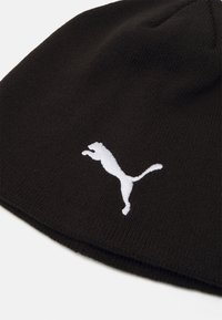 Black knit beanie made of textured fabric, featuring a white embroidered Puma logo. The design is simple and fitted, suitable for cold weather.