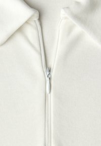 Felpa con cappuccio e cerniera in tessuto morbido color panna. Presenta un colletto appuntito, una texture a coste e una cerniera argento con un cursore bianco.