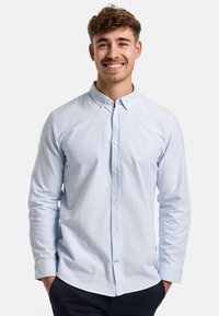 Hellblaues Button-Up-Hemd mit dünnen weißen Streifen, langen Ärmeln und einem Kragen. Verfügt über ein kleines Logo auf der Brust und einen abgerundeten Saum.