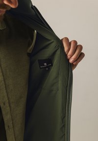 Green jacket made of smooth fabric with zipper closure. Interior features a pocket with a black label reading "STATE OF ART" and size "M."