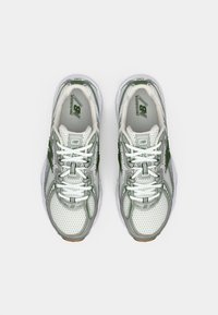 Baskets de sport blanches et vertes avec un design en maille, des accents renforcés, des semelles rembourrées et des lacets blancs. Présente le branding New Balance.