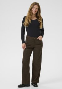 Pantalons en velours côtelé marron à jambes larges avec une taille haute et une fermeture à bouton sur le devant, associés à un haut noir ajusté à manches longues.