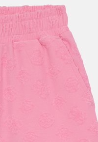 Pantalon de survêtement rose avec un motif texturé de formes circulaires et de diamants. Équipé d'une taille élastique et d'une poche latérale. Matériau doux et léger.
