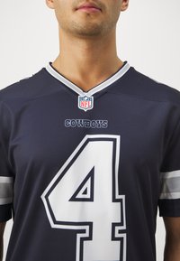 Tengerészeti kék NFL mez fehér és szürke kiegészítőkkel. A 4-es szám, a "COWBOYS" felirat és az NFL logó látható a galléron. Simás anyagból készült.