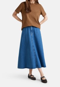 Hnědé tričko s krátkým rukávem v kombinaci s dlouhou modrou džínovou sukní a černými tkanými botami. Sukně má přední šev a lemované okraje.