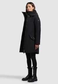 Mustikas isolatsiooniga jope, millel on kõrge krae, lukuga sulgemine, küljetaskud ja kerge läike. Kandmiseks mustade retuuside ja pahkluusaabaste peal.