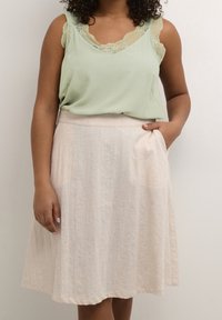 Light green sleeveless top with lace trim, paired with a cream-colored, knee-length A-line skirt featuring side pockets and a textured finish.