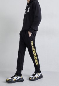 Černá mikina s bílým textem, spárovaná s černými kalhotami s obilným vzorem na boku. Černobílé vzorované tenisky.