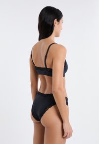 Schwarz spitzenbesetzter BH und passende, hoch taillierte Slip. Weicher, glatter Stoff, schlankes Design, detaillierte Spitzenakzente an den Rändern, minimalistischer Stil.