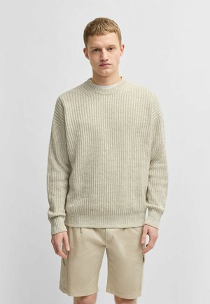 Maglione a coste beige chiaro con scollatura rotonda e maniche lunghe, abbinato a pantaloni corti khaki chiaro. Motivo a maglia testurizzato su tutta la superficie.