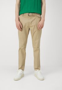 Beżowe bawełniane chinosy o slim fit, z paskiem w talii i kieszeniami bocznymi, w połączeniu z białymi sneakersami. Teksturowany zielony sweter dzianinowy.
