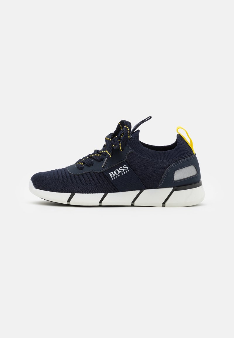 Baskets tricotées bleu marine avec semelle blanche segmentée, lacets noirs et jaunes, boucle jaune au talon et logo BOSS Hugo Boss sur le côté.