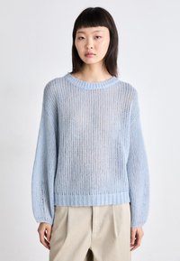 Pull en tricot bleu clair avec une coupe ample, des manches larges, un ourlet côtelé et une texture ajourée. Associé à un pantalon beiger.