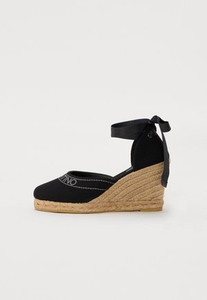 Espadrille en toile noire avec un talon en jute, dotée d'un lien à la cheville en ruban et d'un bout arrondi avec des détails de couture grise.