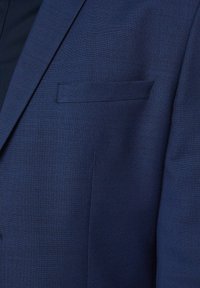 Granatowa marynarka o fakturowanym materiale. Pojedyncza kieszeń na piersi po lewej stronie. Dopasowany krój z precyzyjnymi detalami szwów.