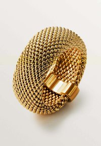 Pulsera de manilla de malla dorada con un diseño texturizado y tejido, y un cierre pulido. Presenta una silueta redondeada y sin costuras.