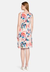 Robe sans manches à motifs floraux, présentant un fond pastel clair avec de grandes fleurs roses et bleues, une forme légèrement évasée et une fermeture éclair dissimulée au dos.