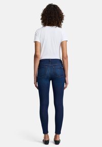 Mörkblå smala jeans med hög midja, med två bakfickor och en mjuk, stretchig textur. Kombinerade med en enkel vit t-shirt.