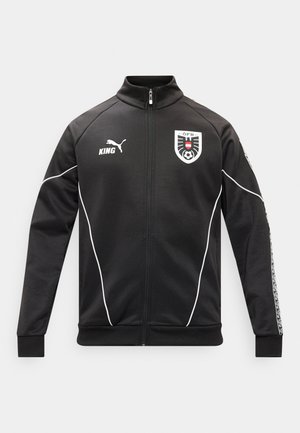 Must zipuga spordijakk valgete triipudega, Puma logo ja "KING" tekst paremal rinnal, Austria Jalgpalliliidu embleem vasakul rinnal.