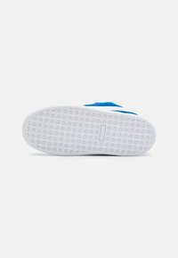 Zapatilla azul con una suela de goma blanca y plana, patrón texturizado en la parte inferior, y parte superior de textil azul con perforaciones para transpirabilidad.