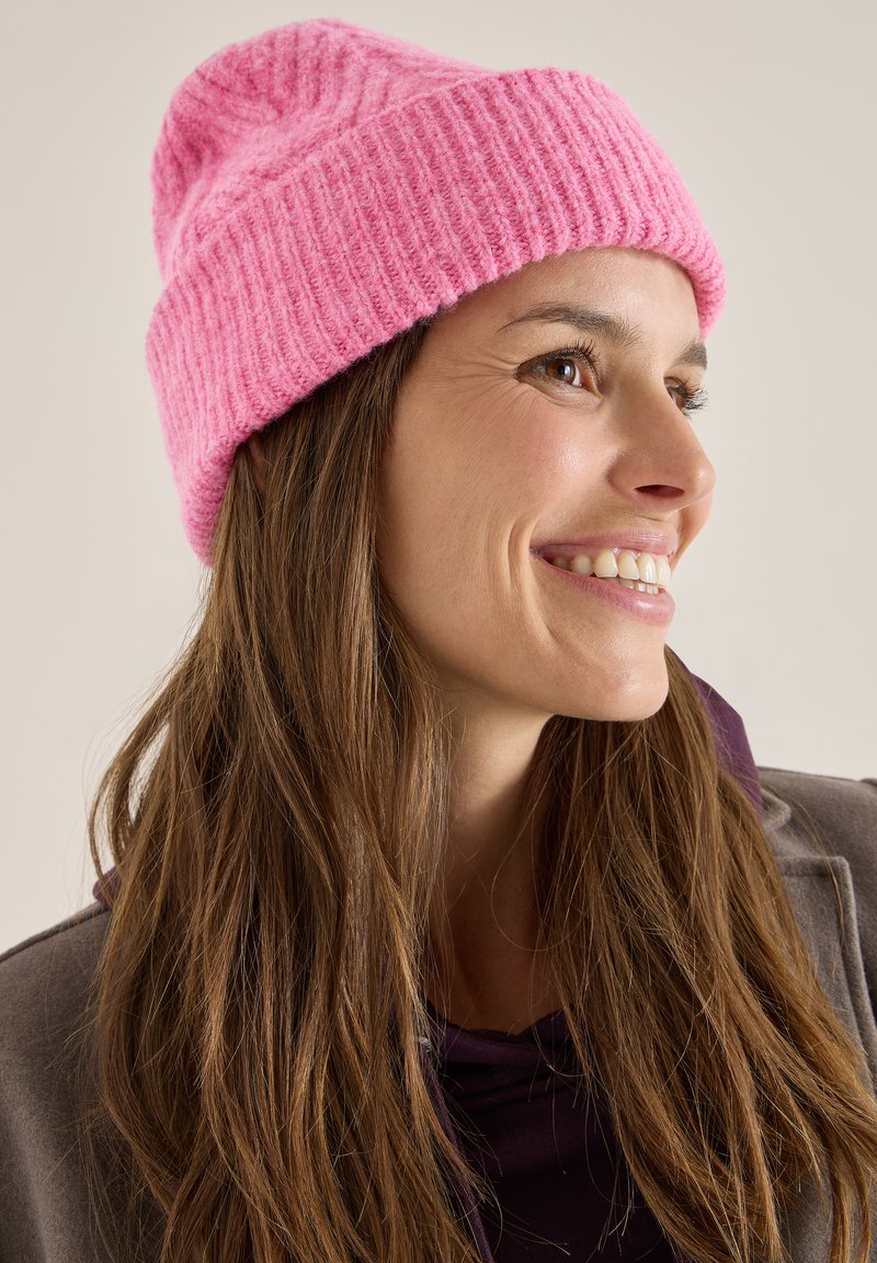 Gorro de lana rosa de punto con textura acanalada, forma ajustada y parte superior ligeramente caída. Material cálido adecuado para climas frescos.